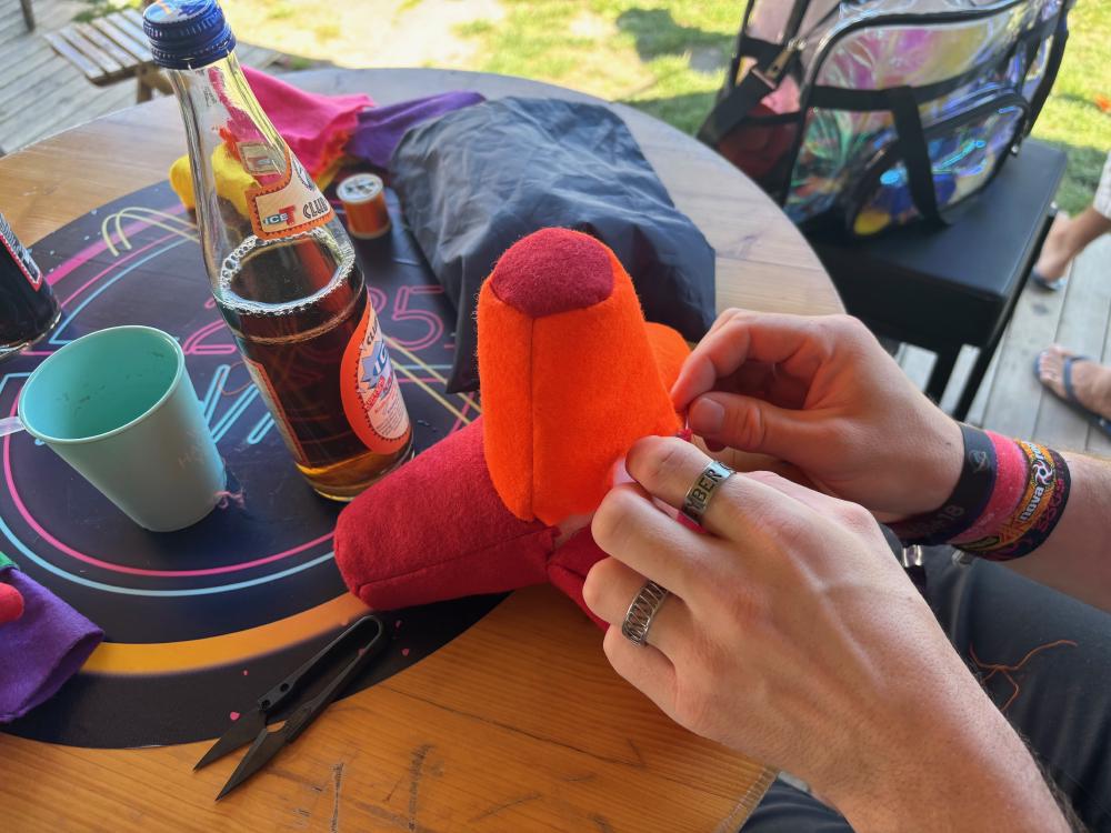 A red and orange tetrapod in the process of being finished by hand. On the table is a club mate bottle and a sticker with the WHY2025 logo.