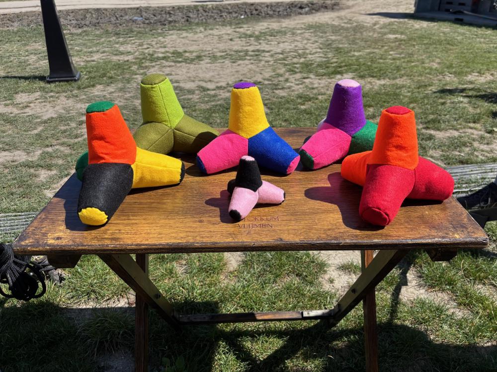 A collection of multi-colored felt tetrapods sitting on a wooden table in a field in the sun.