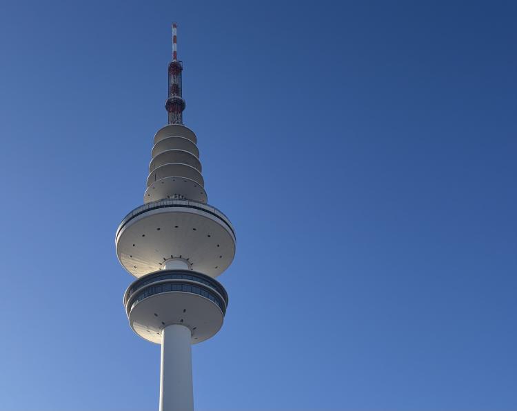 A photo of the top of a white tower with a series of disc-shaped decks, topped by a red and white mast.